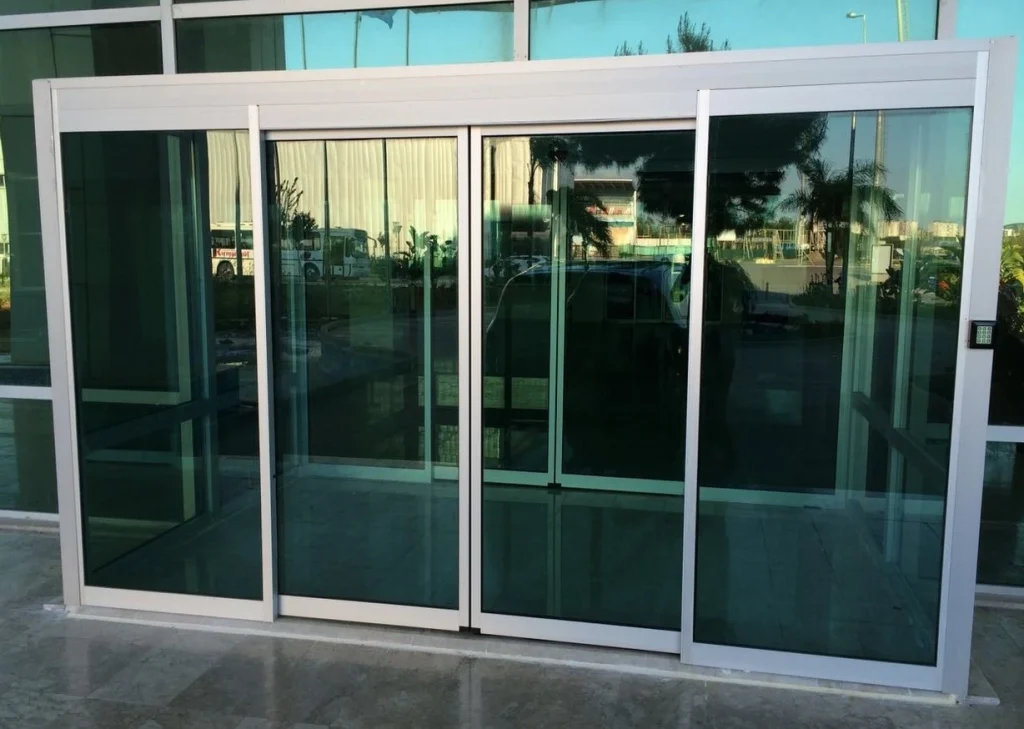 Industrial 53 Puerta automática corrediza de dos hojas con apertura lateral, hechas con marco de aluminio y vidrio.