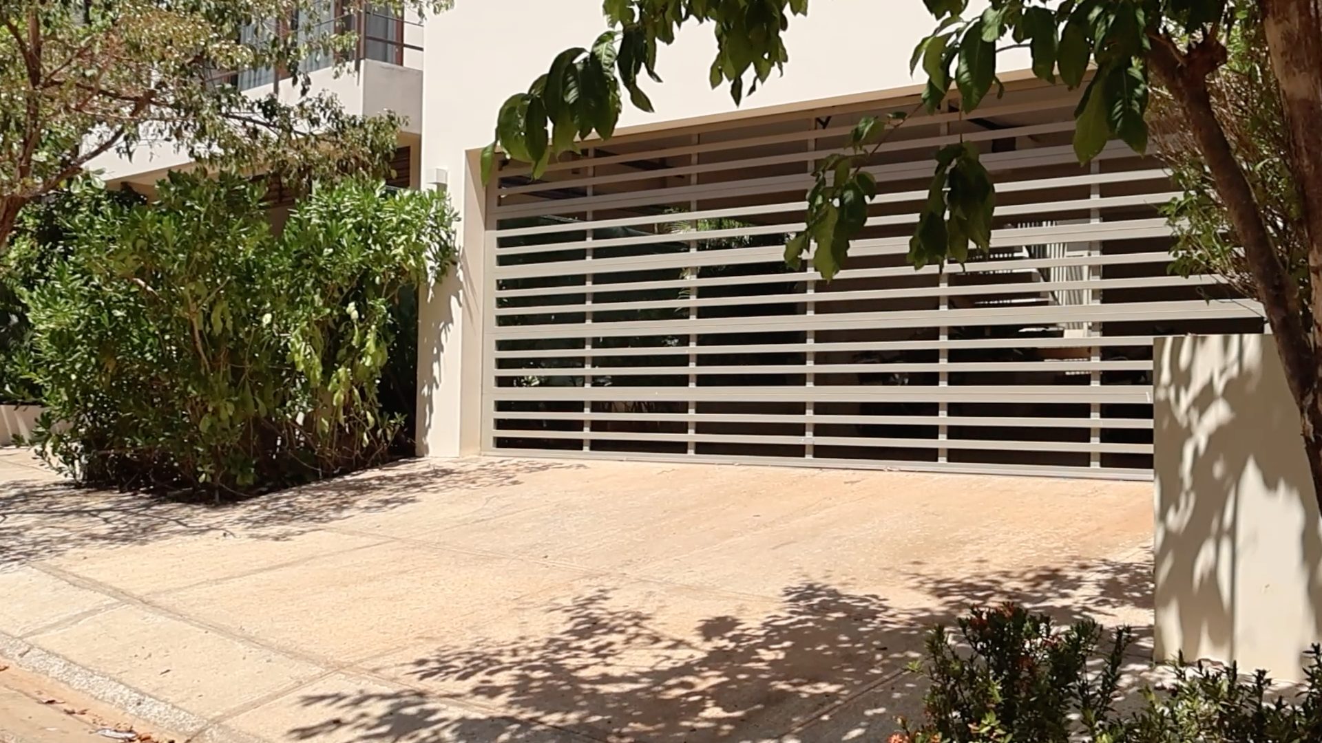 Vista frente diagonal de una casa con portón de entrada estilo seccional de barrotes horizontales con separaciones entre estos.